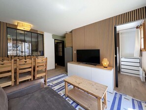 Sala de estar moderna com televisão de tela plana, móveis de madeira e piso estampado.