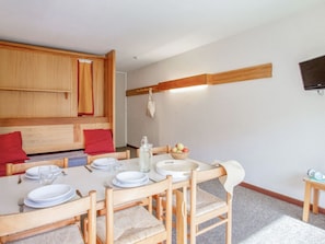 A dining area with a wooden table set for four, chairs with woven seats, a bowl of fruit, and a television mounted on the wall. - Studio with South balcony - 4 guests (Saint-Chaffrey)