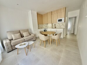 A modern living room with a sofa, a small round table, and a dining area with chairs. - .Bajo B (Nerja)