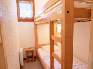 Ein Schlafraum mit Etagenbetten, einem kleinen Holzschemel und einem Fenster mit dekorativem Rahmen.