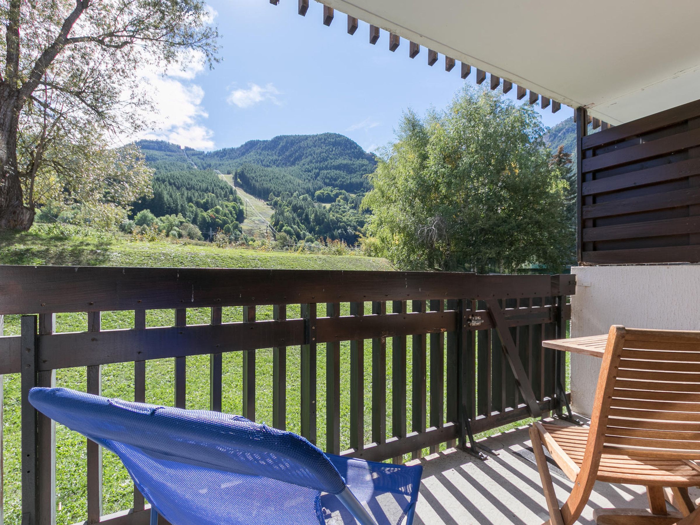 Ein Balkon mit Holzgeländer, einem blauen Stuhl und einem Holztisch.