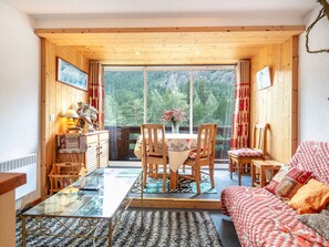 A cozy room with a wooden ceiling, a glass table, a sofa, and a view of a forest through large windows. - Pleasant studio, parking - mountain view (La Salle-les-Alpes)