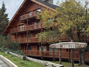 A multi-story wooden lodge with balconies, surrounded by trees and a stone wall. - Renovated apartment near slopes - 6 guests (Méribel)