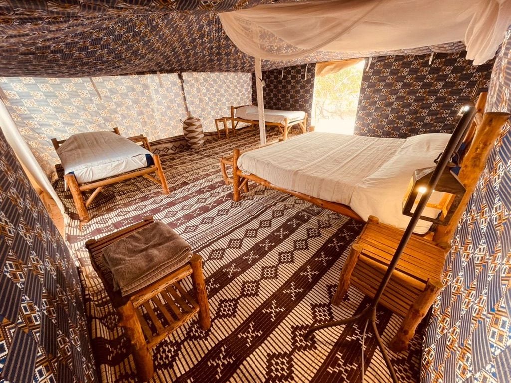 A room with a bed, two wooden chairs, a small table, and a canopy bed.
