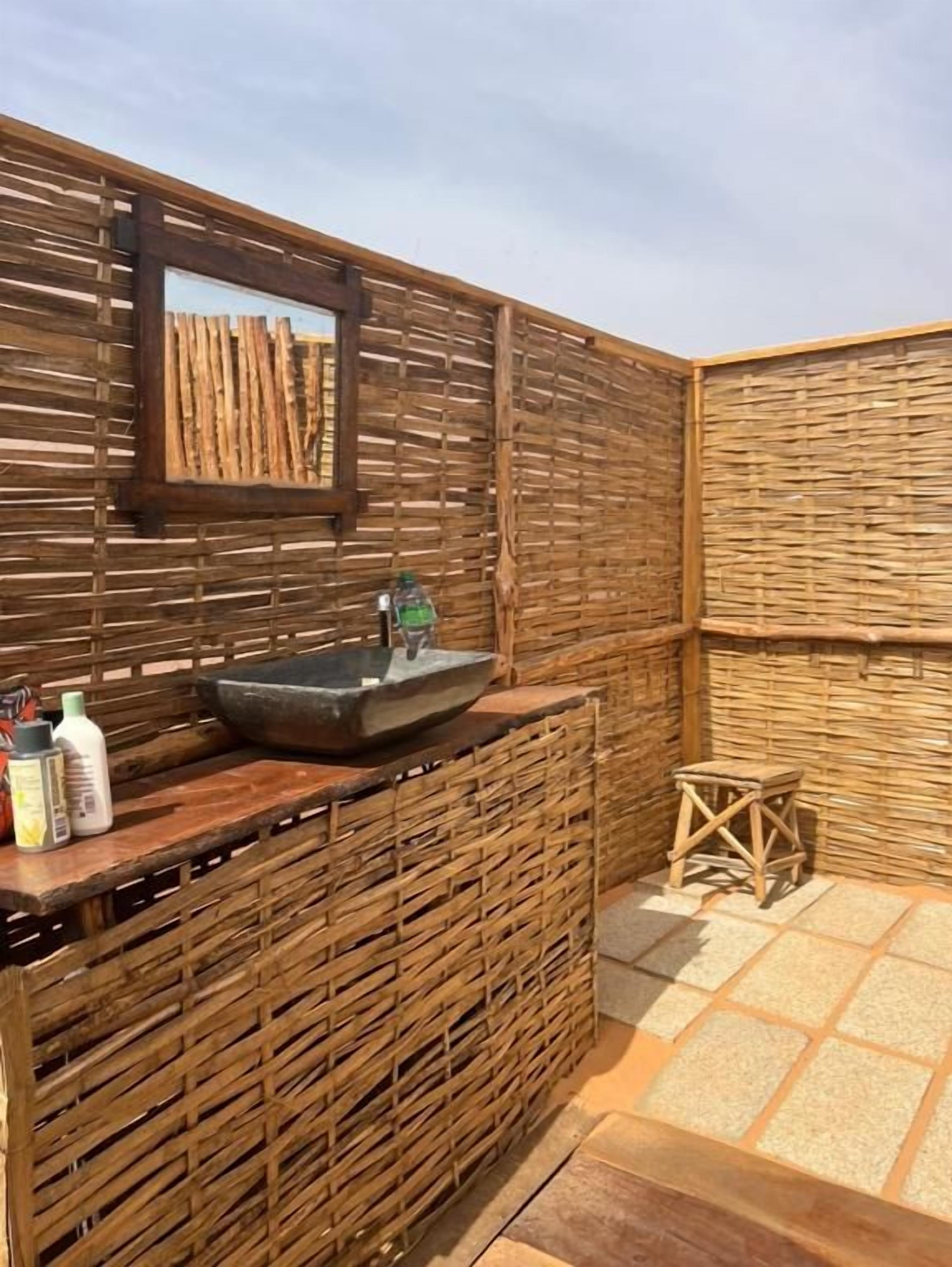 Un baño con un lavamanos de piedra, paneles de pared de madera, un taburete pequeño y un espejo.