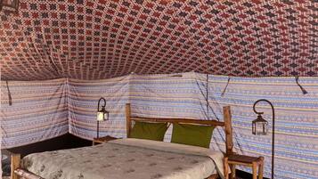 A tent with a patterned fabric interior, a wooden bed frame, and two wall-mounted lanterns.