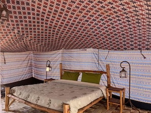 A tent with a patterned fabric interior, a wooden bed frame, and two wall-mounted lanterns. - Camp Rêve de Nomade (Lompoul)