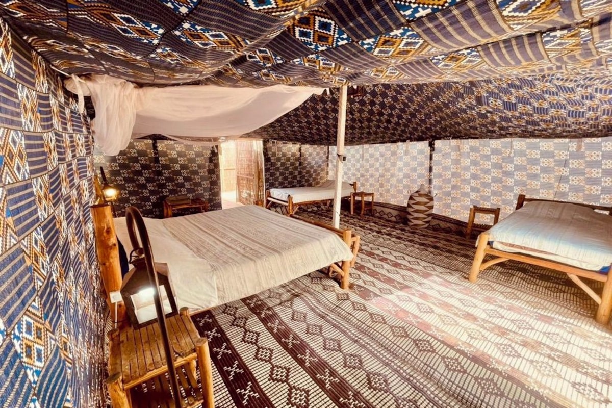 Una habitación tipo tienda con una cama, dos sillas y paredes con un diseño estampado.