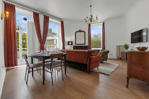 A dining area with a table set for four, a sofa, a TV mounted on the wall, and a view of the outside through large windows. - Luxury South Kensington Retreat (London)