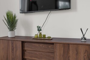 A flat-screen TV mounted on a wall above a wooden cabinet with a potted plant and decorative items on the cabinet's surface. - Luxury South Kensington Retreat (London)