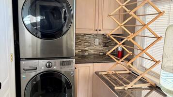 A laundry area with two stacked front-loading washers and dryers, wooden drying racks, and a tiled backsplash.
