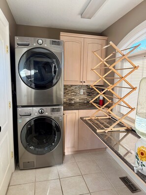 Un espace buanderie comprenant deux machines à laver et deux sèche-linge à chargement frontal superposés, des étendoirs en bois et un pare-feu en carrelage.