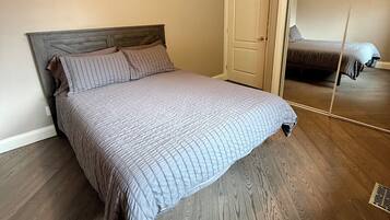 A bedroom with a bed, wooden flooring, a door, and a mirror.
