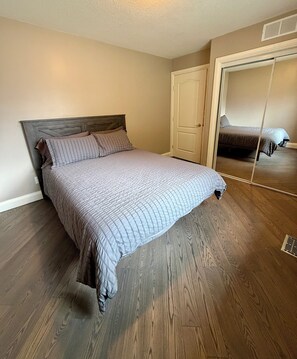 A bedroom with a bed, wooden flooring, a door, and a mirror. - Spacious 3BR Knox Mountain Home | 5 Min to Downtown (Kelowna)