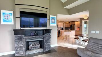 A living room with a fireplace, a sofa, and a kitchen in the background.