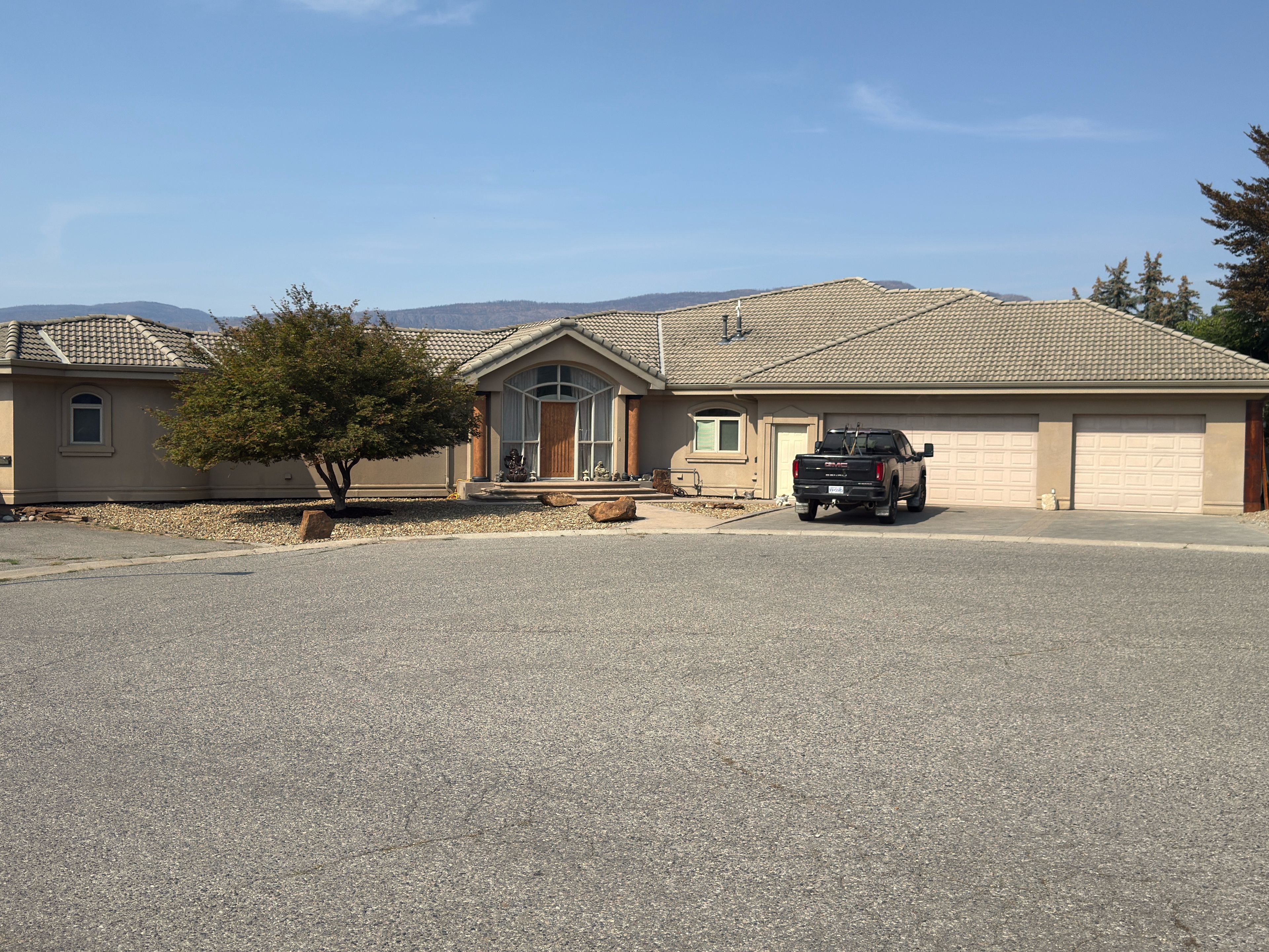 A residential property with a garage, a driveway, and a tree in the foreground.