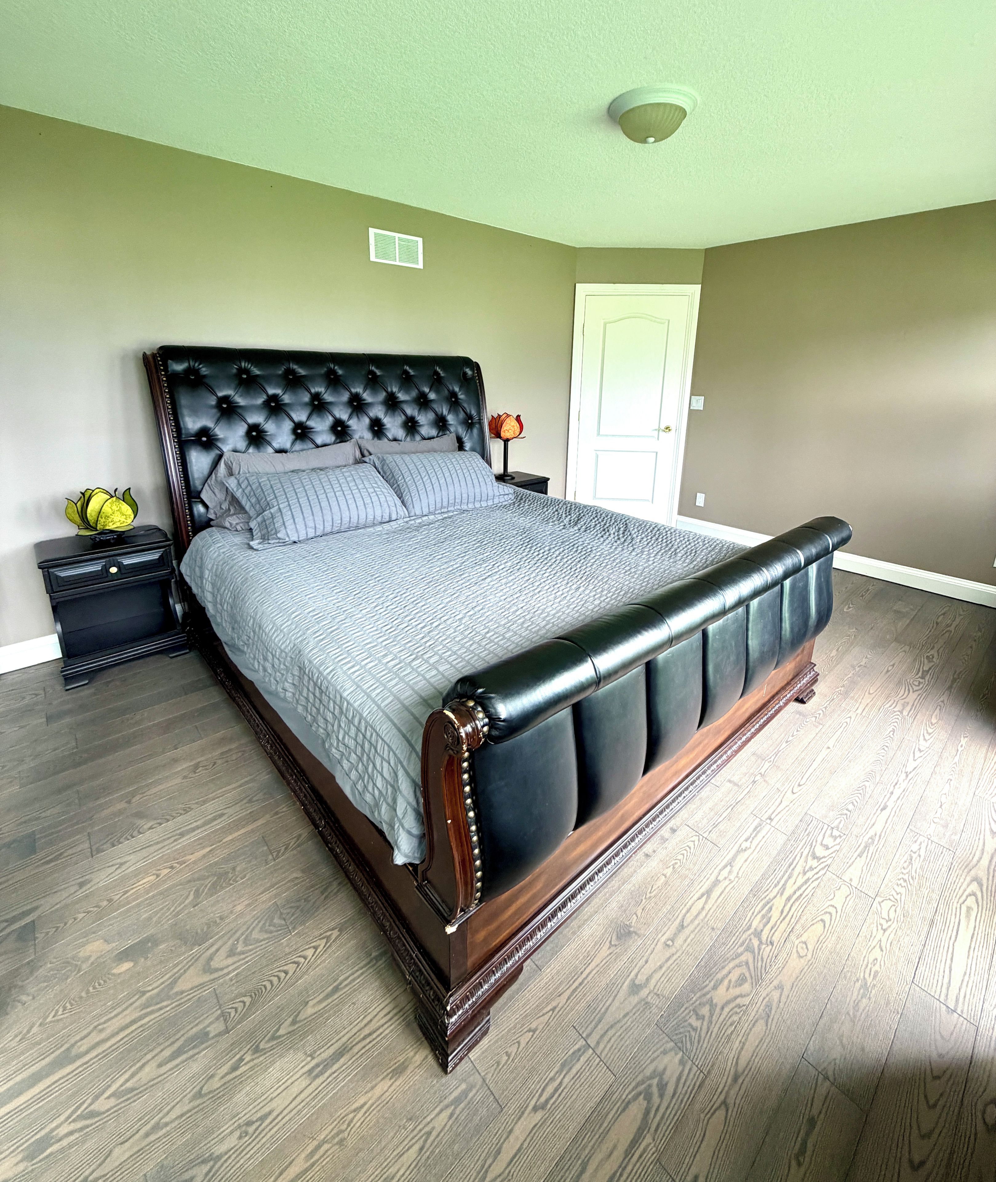 A bedroom with a large bed, a nightstand, a lamp, and a door.