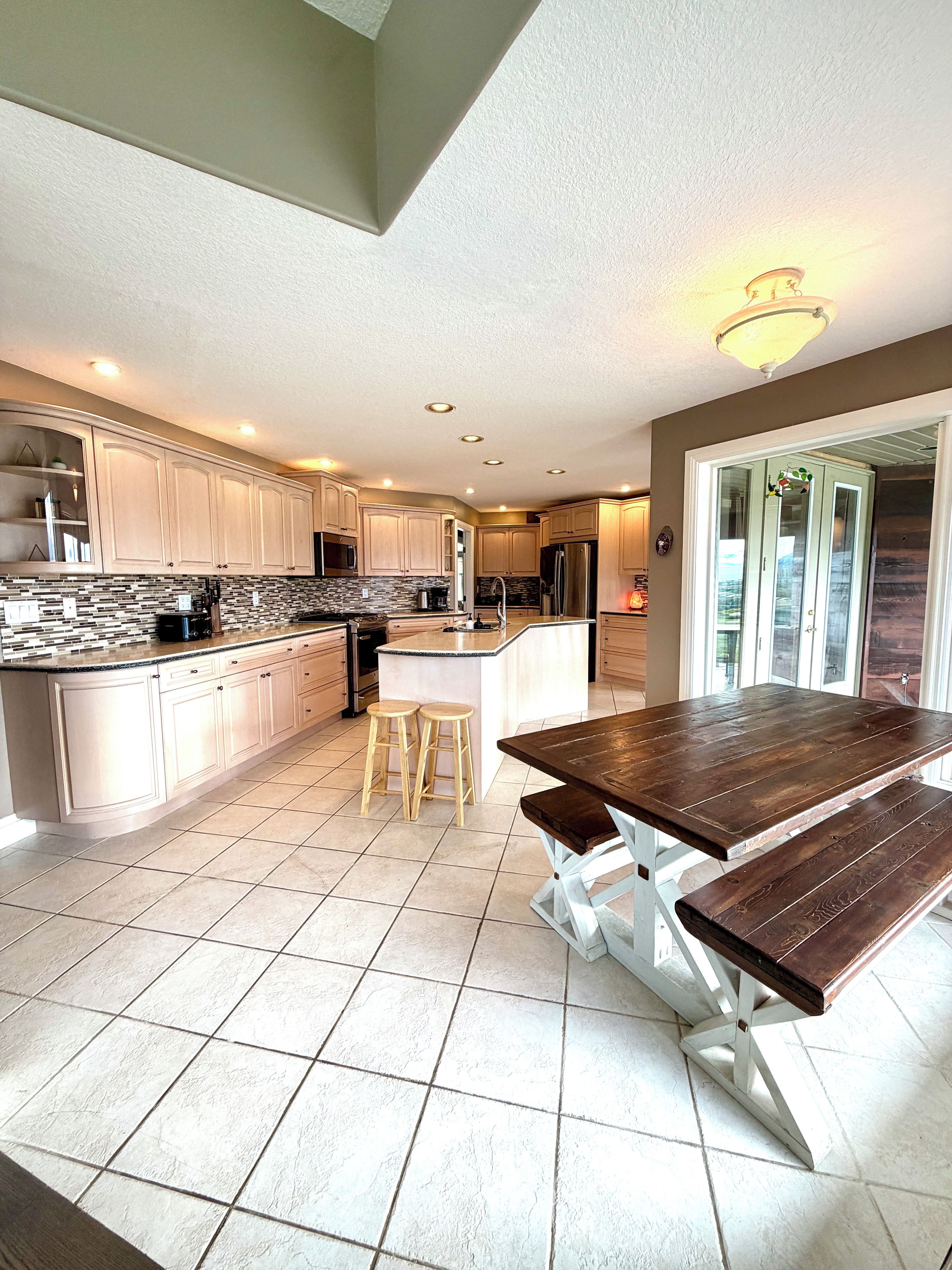 A modern kitchen with a central island, bar stools, and a wooden dining table.