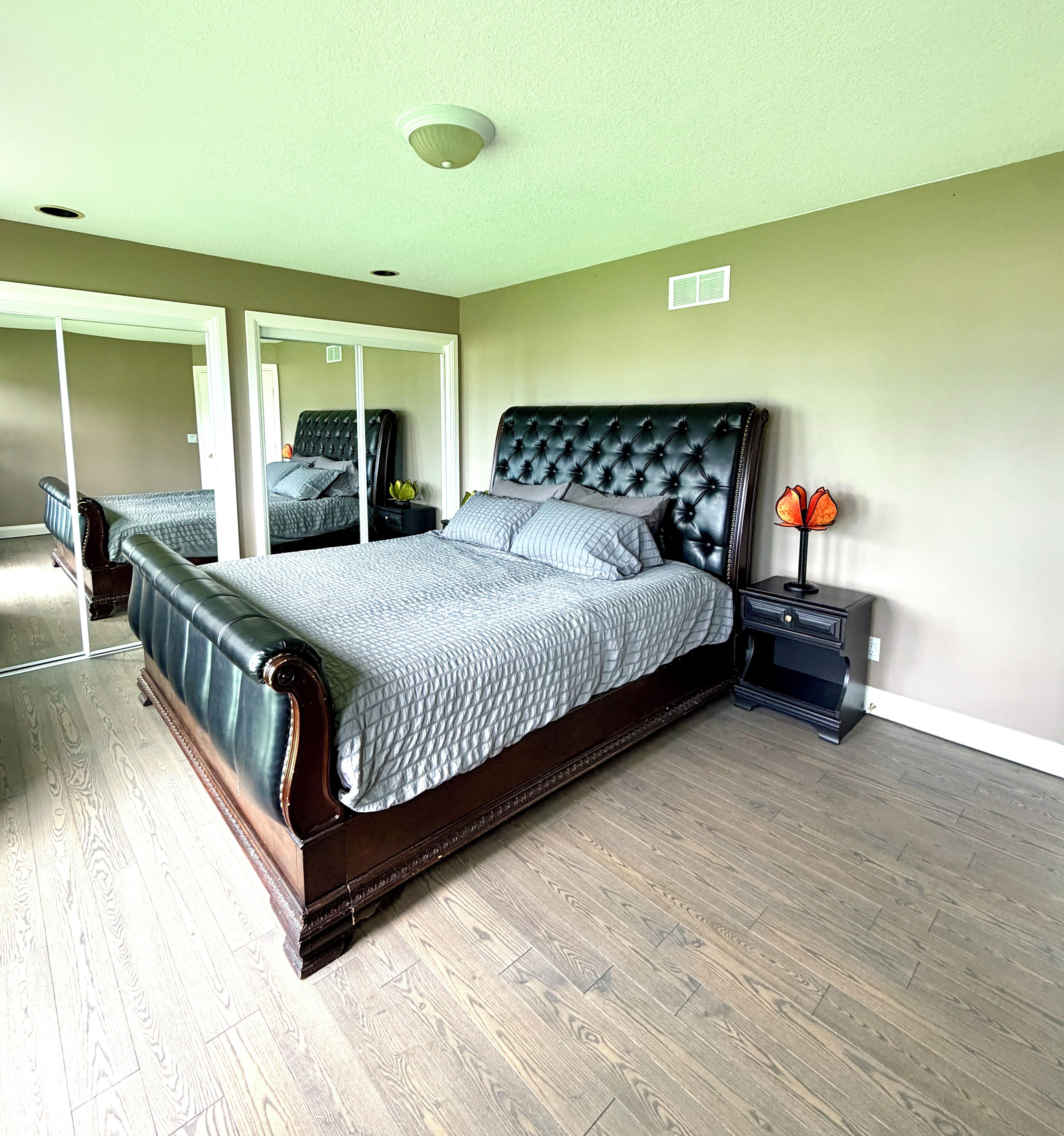 A bedroom with a large bed, a nightstand, a mirror, and a ceiling light.