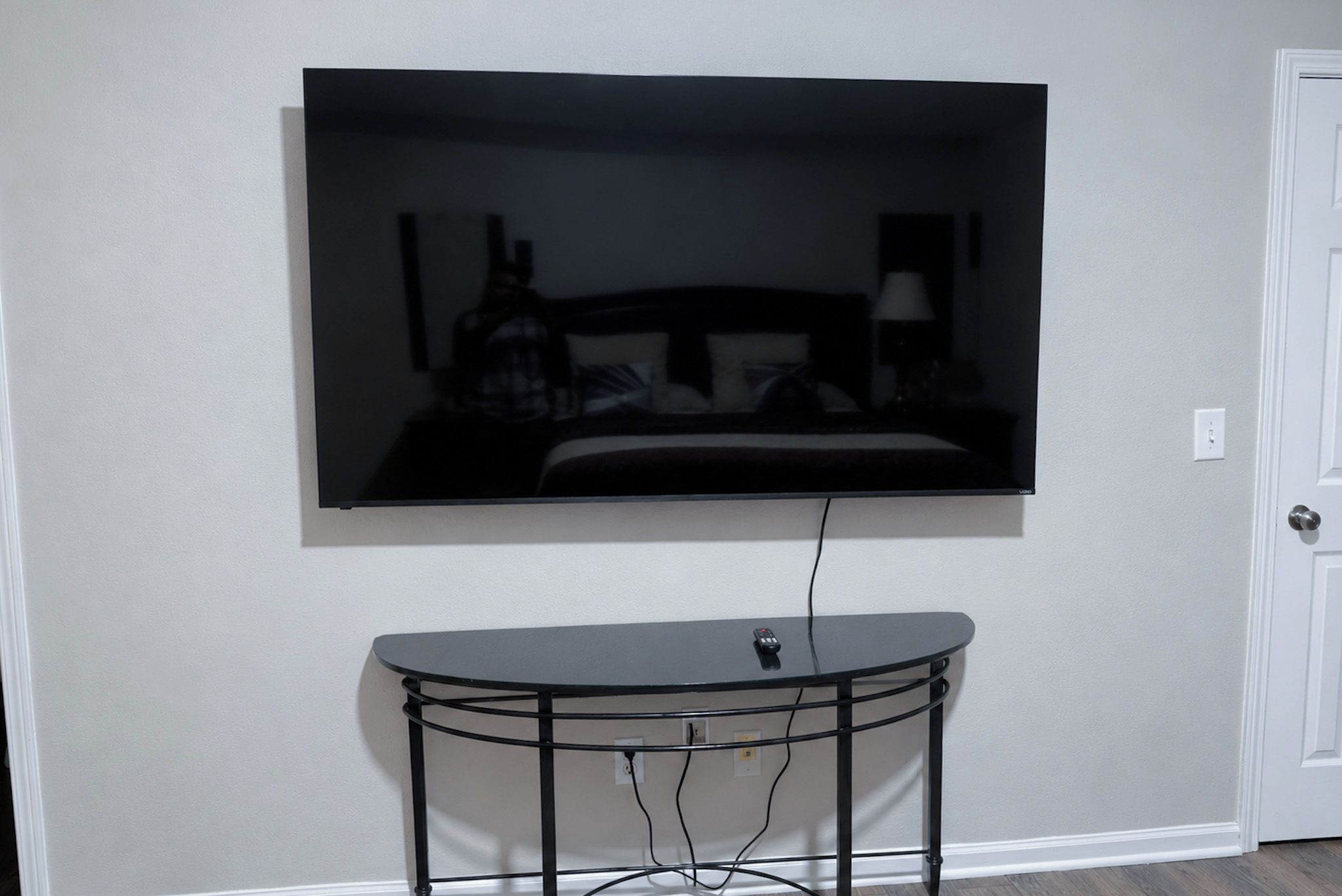A television mounted on a wall above a small, round, metal-framed table with a remote control on it.