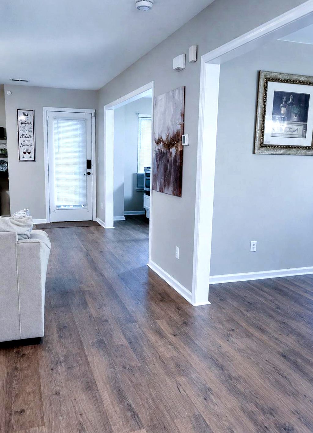A spacious living room with hardwood flooring, a beige sofa, and a hallway leading to other rooms.
