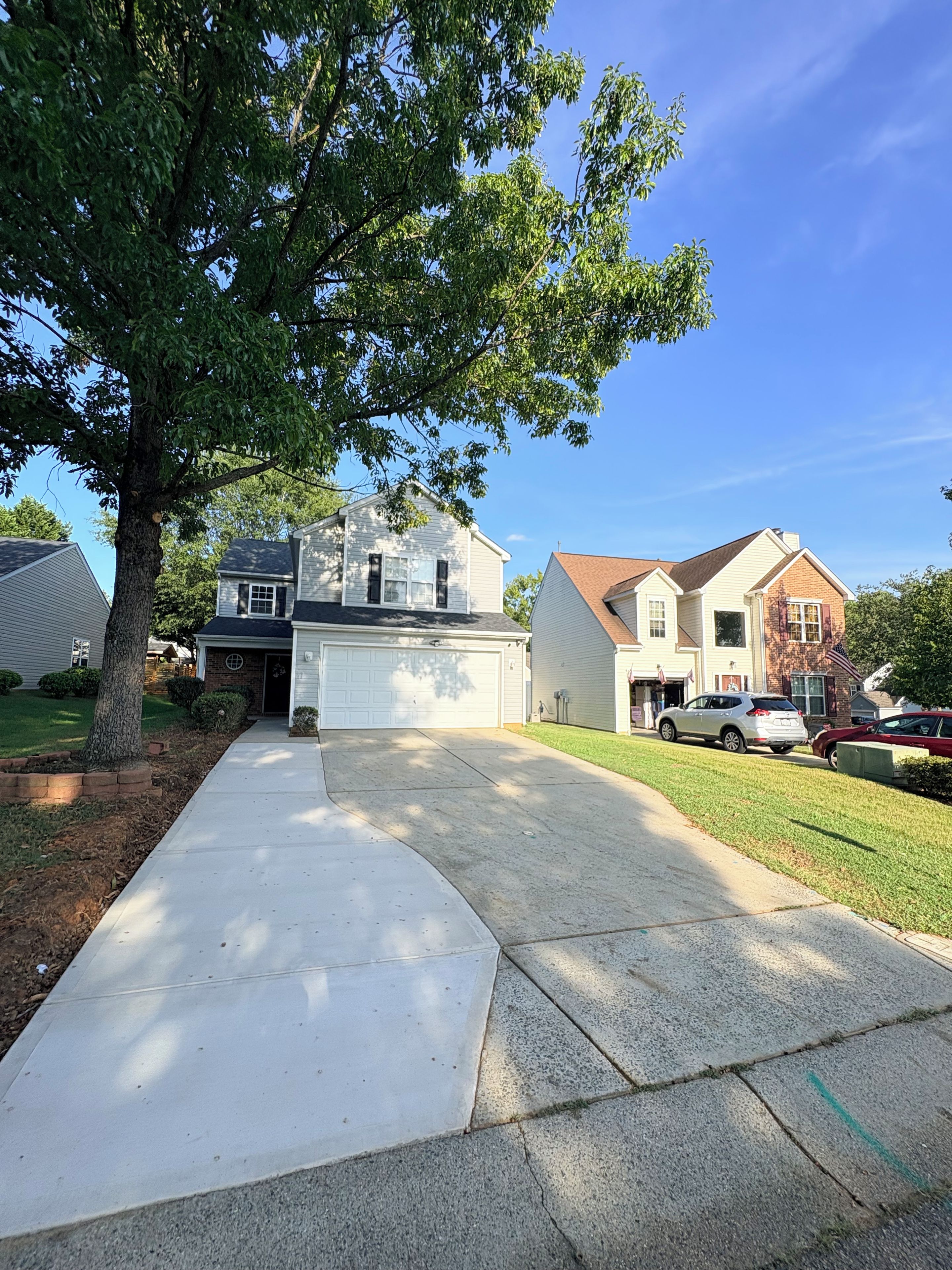A residential driveway with a garage, a lawn, and a tree.