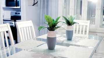 Un comedor con mesa de vidrio, sillas blancas y dos plantas en macetas.