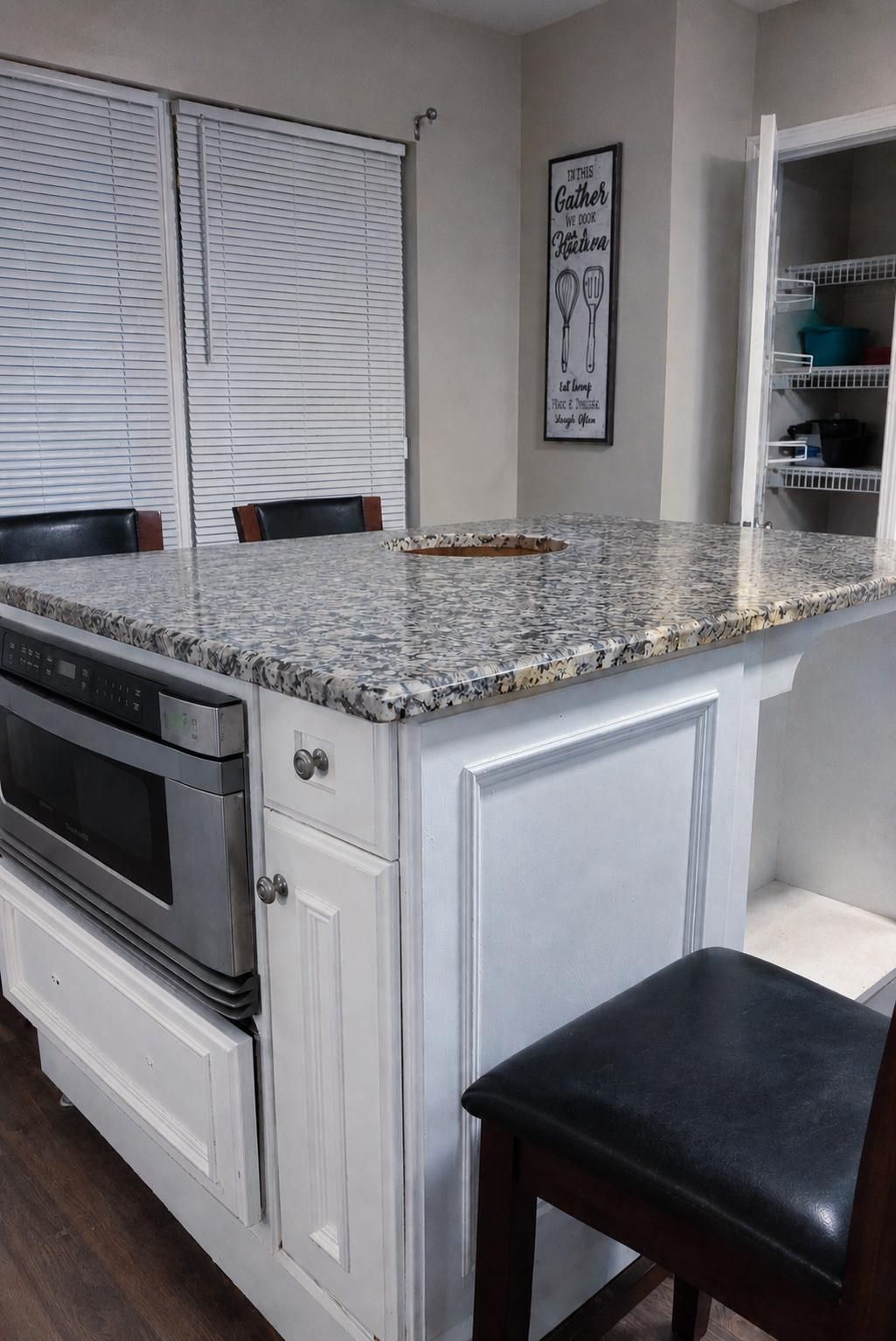 A kitchen with a granite countertop, white cabinetry, a built-in oven, and a dining area with a chair.
