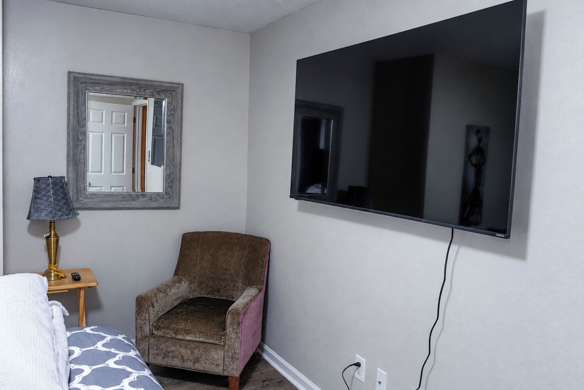 A bedroom with a bed, a chair, a lamp, a TV, and a mirror.