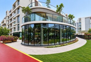 A modern building with a curved glass facade, surrounded by a well-maintained lawn and flower beds. - HAVN - Spacious studio in Torino, Arjan (Dubai)