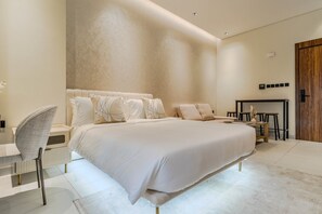 A modern bedroom with a large bed, a bedside table, a chair, and a small desk with a chair. - HAVN - Spacious studio in Torino, Arjan (Dubai)
