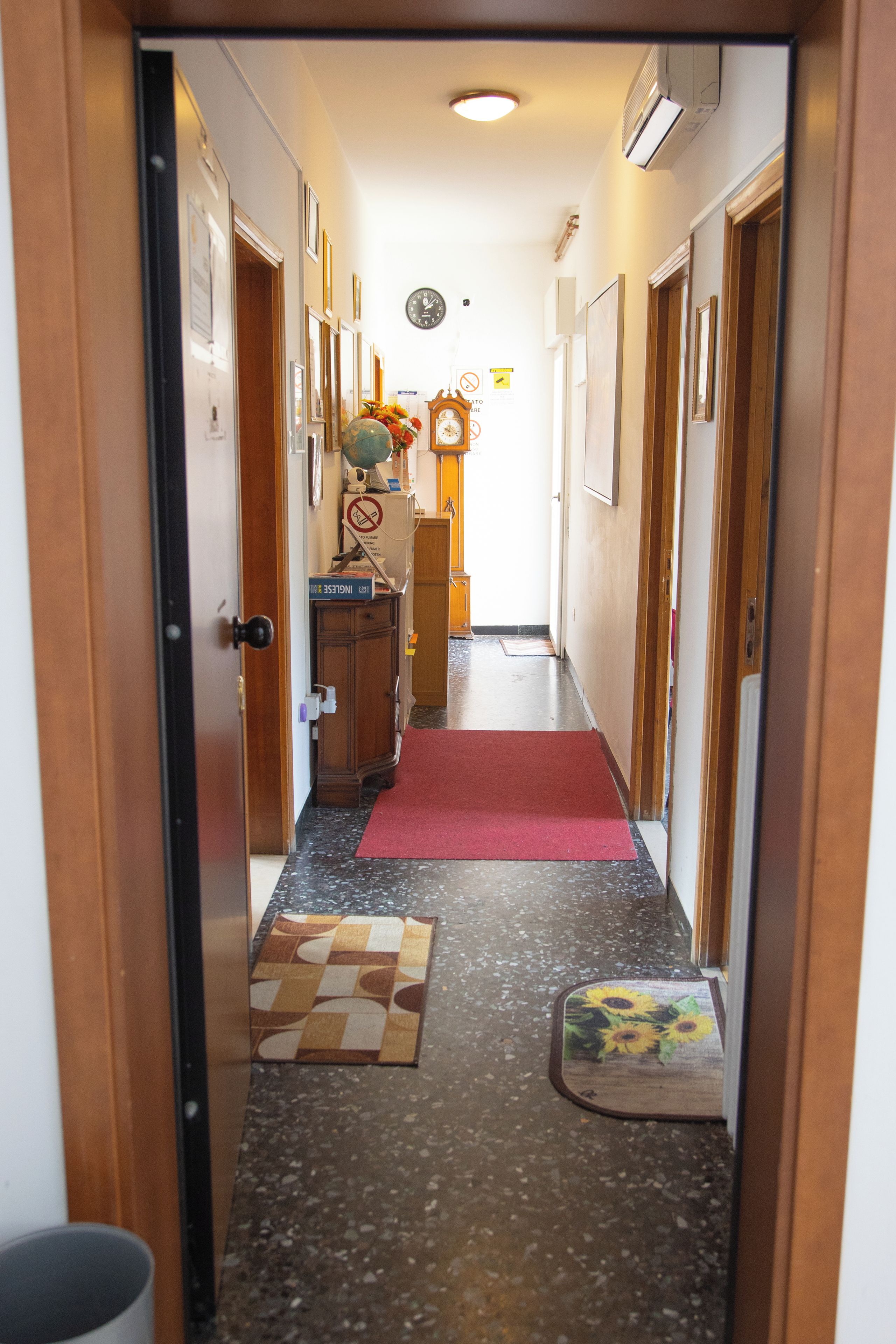 A hallway with wooden doors, a clock, and a red carpet leading to a room.