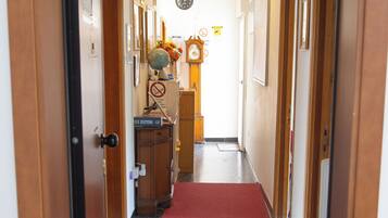 A hallway with wooden doors, a clock, and a red carpet leading to a room.