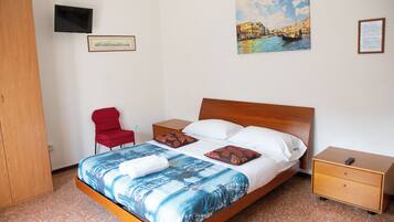 A hotel room with a bed, a TV, a red chair, a wooden wardrobe, and a painting of a cityscape.