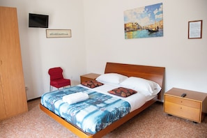 A hotel room with a bed, a TV, a red chair, a wooden wardrobe, and a painting of a cityscape. - Vrbo Property (Venezia)