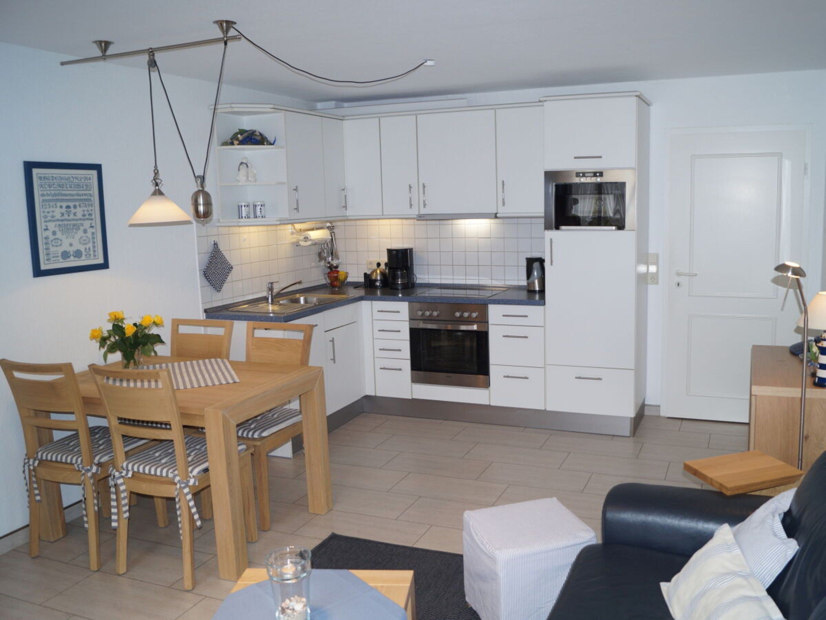 A compact kitchen with white cabinets, a stove, and a microwave. There is a dining area with a wooden table and chairs.