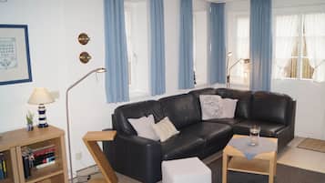 A living room with a black leather sofa, a wooden coffee table, a bookshelf, and a lamp.