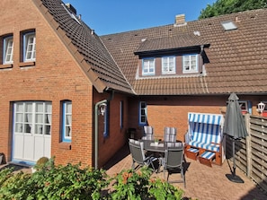 A two-story brick house with a tiled roof, a patio with a table and chairs, and a striped beach chair set. - Holiday Apartment With 1 Bedroom (Wyk auf Foehr)