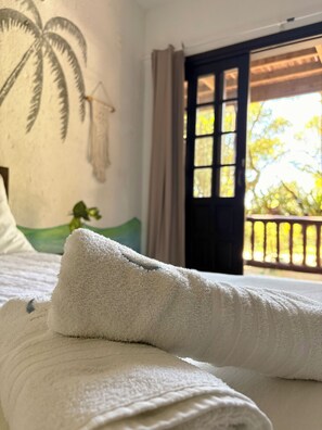A bed with white linens and a wall mural of palm trees.