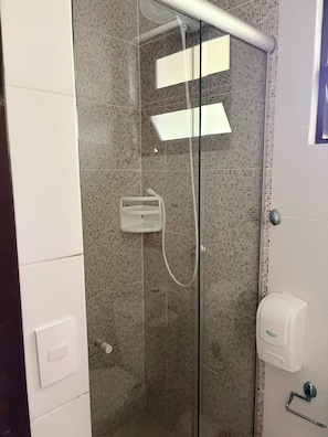 Cabina de ducha con paredes de vidrio, ducha de mano, dispensador de jabón y toallero en la pared.