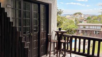 Un balcón de madera con una mesa y sillas, una puerta de madera oscura y vistas a una zona residencial.