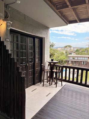 Un balcón de madera con una mesa y sillas, una puerta de madera oscura y vistas a una zona residencial.