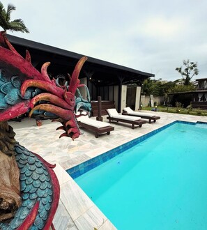 Una piscina con sillones de descanso y una gran escultura de dragón.
