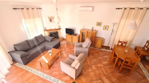 Uma sala de estar com sofá, poltronas, mesa de centro, televisão e lareira.