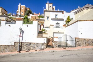 Vista da rua com um edifício branco, uma parede de pedra e um portão de metal.