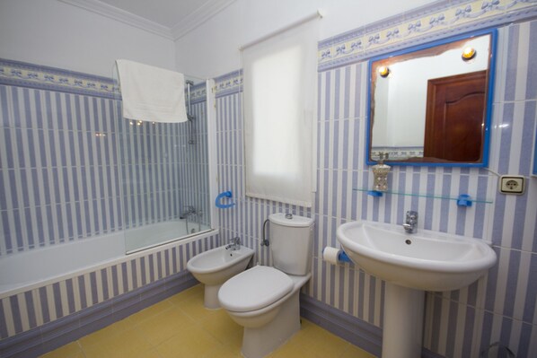 Un baño con bañera, dos inodoros, un lavabo y un espejo.