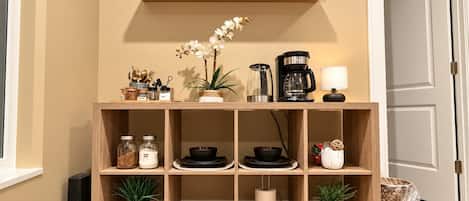 A wooden shelf unit with kitchenware, a coffee maker, and a welcome sign.