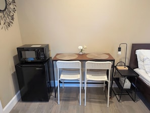 Una habitación compacta con kitchenette, que incluye un refrigerador, microondas y una pequeña mesa con dos sillas.