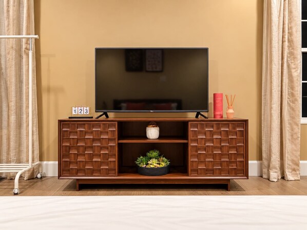 A flat-screen TV on a wooden TV stand with a calendar, a small plant, and decorative items.