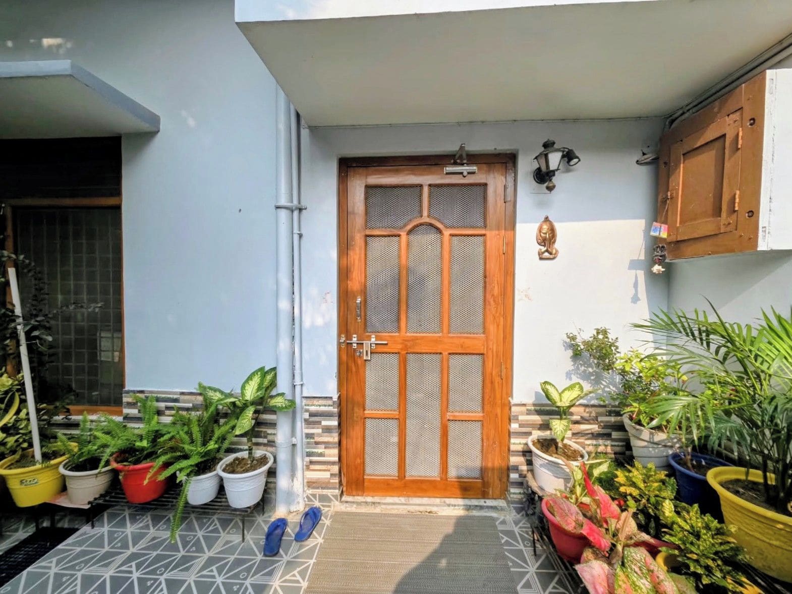 A residential entrance with a wooden door, potted plants, and a tiled floor.